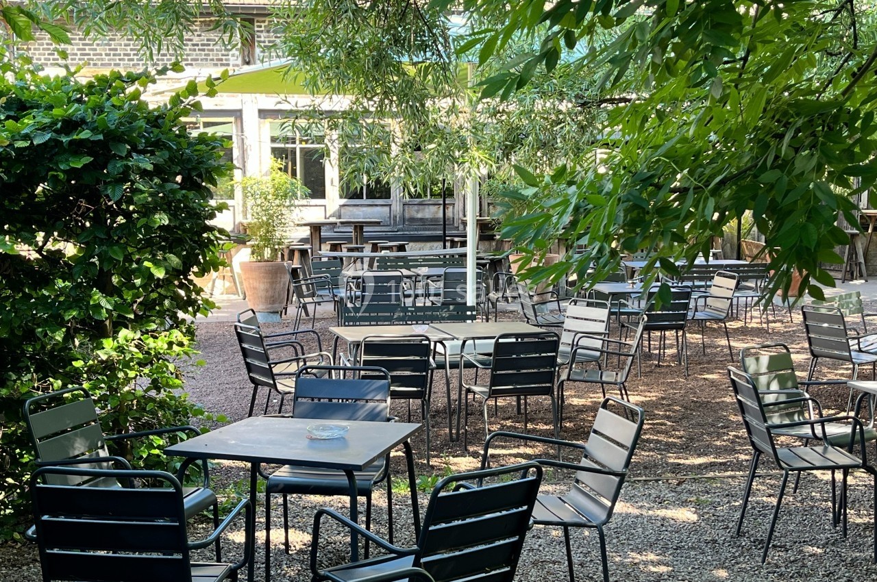 Terrasse extérieure ombragée avec des tables et des chaises en métal, entourée de verdure.