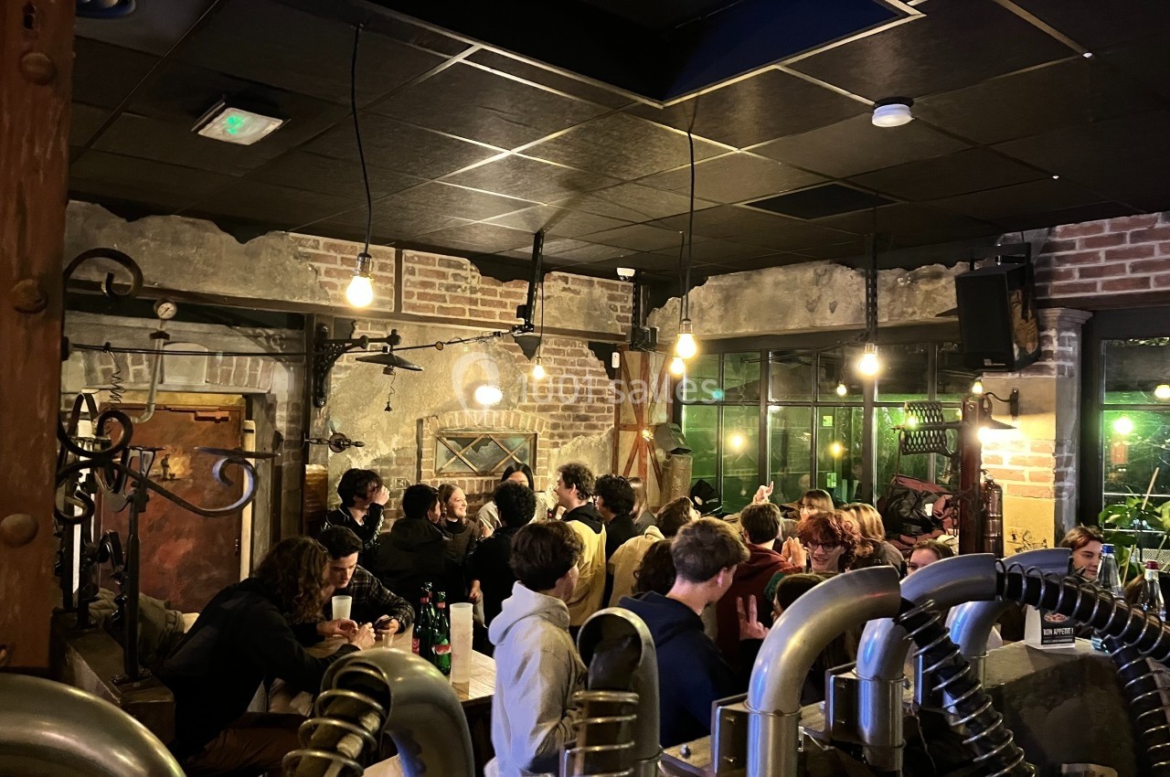 Groupe de personnes discutant et partageant un moment convivial dans un bar à l'ambiance industrielle et chaleureuse.