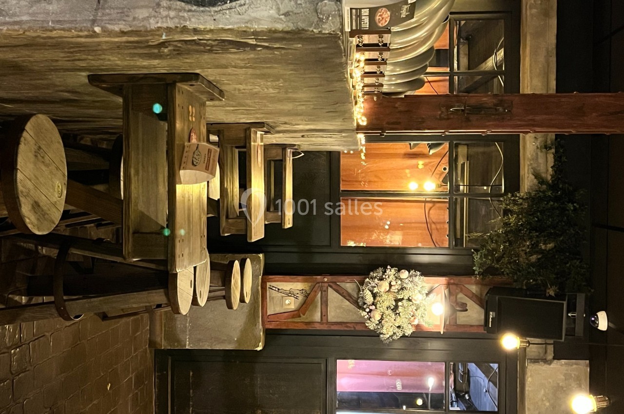 Intérieur d'un bar avec des tables et tabourets en bois, éclairage chaleureux et décoration murale.