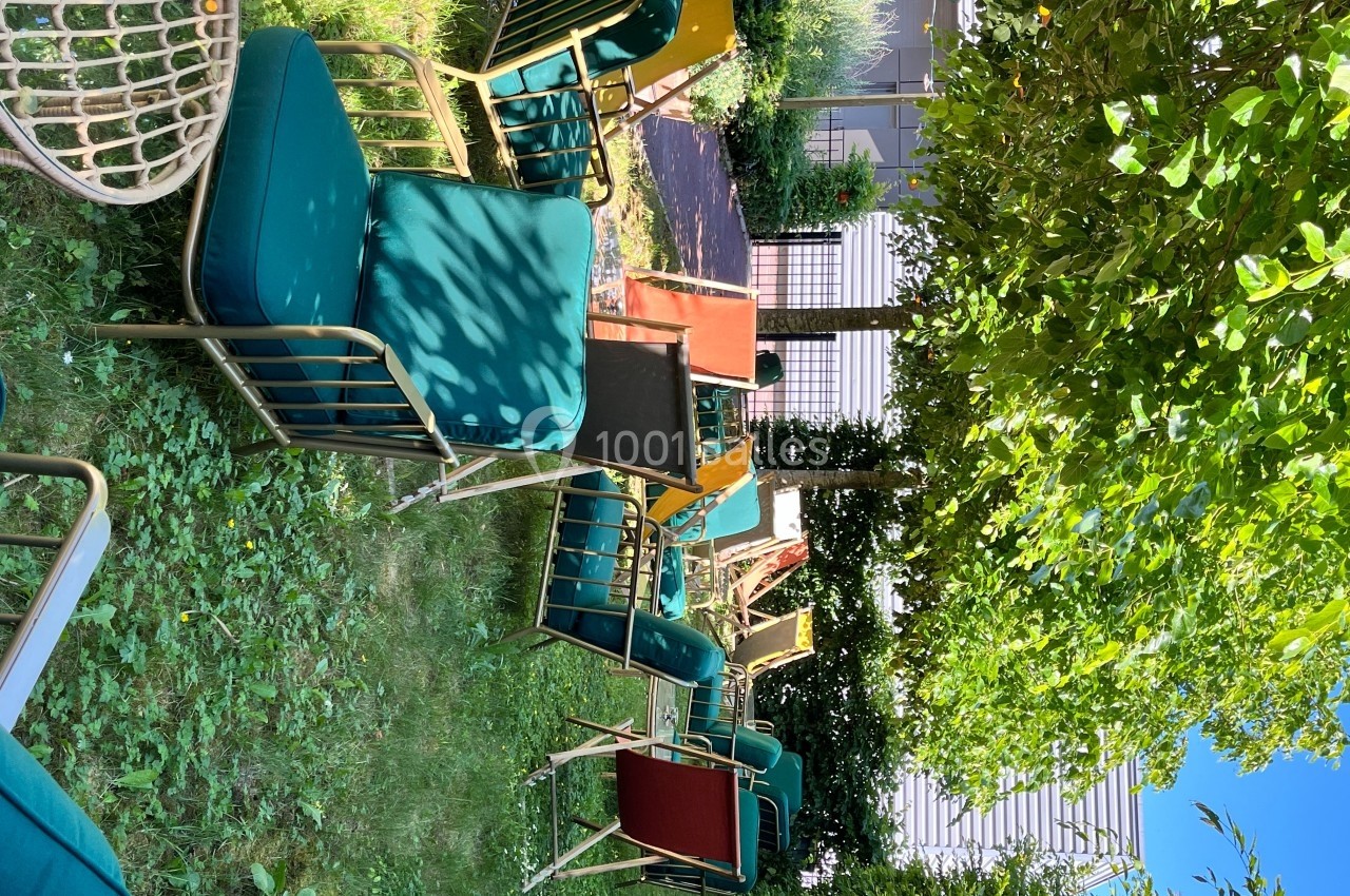 Des chaises longues colorées disposées sur une pelouse ombragée entourée de végétation et de bâtiments modernes.