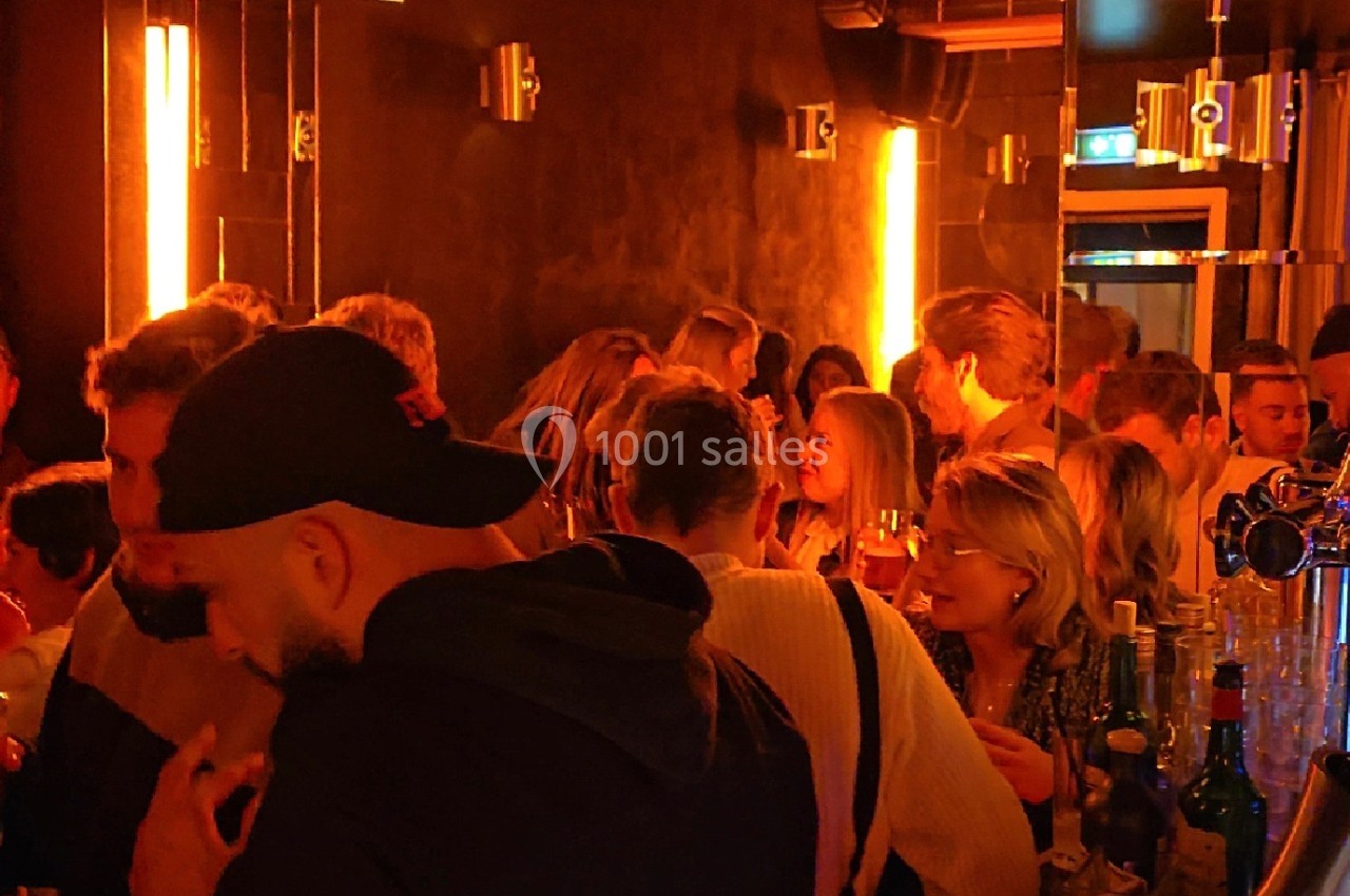Groupe de personnes dans un bar animé, éclairé par des lumières chaudes, avec des bouteilles visibles au premier plan.