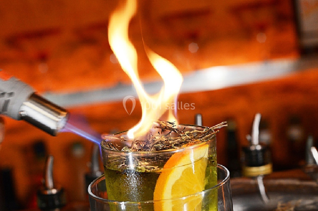 Un cocktail enflammé avec une tranche d'orange, flambé à l'aide d'un chalumeau dans un bar.