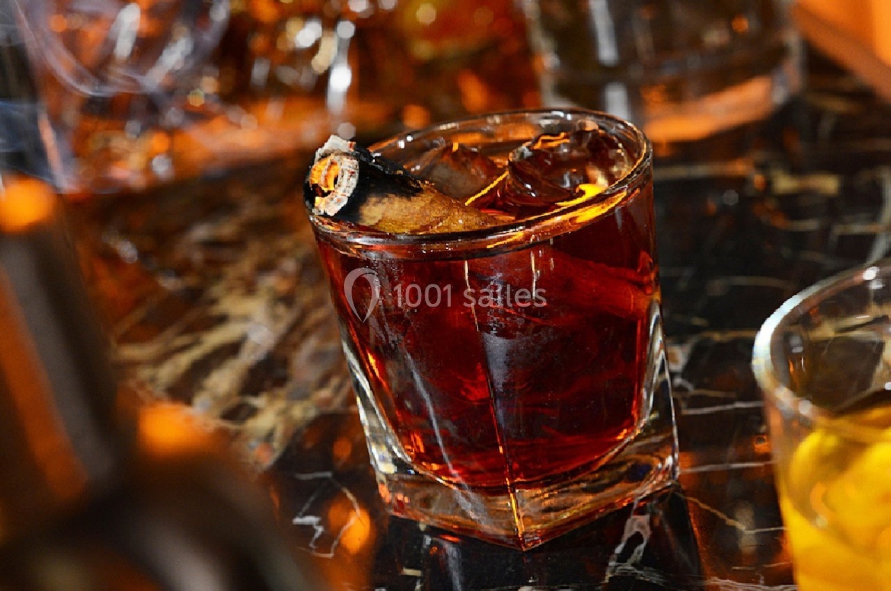 Verre de cocktail ambré garni d'un zeste d'orange brûlé, posé sur une table en marbre sombre.