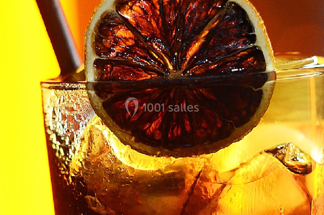 Verre de boisson froide avec glaçons, décoré d'une tranche d'orange séchée et une paille, sur fond jaune lumineux.