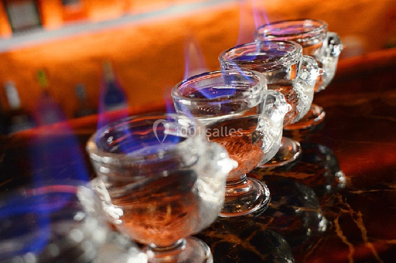 Quatre verres enflammés alignés sur un comptoir en bois sombre dans un environnement de bar.