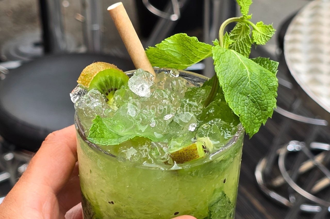 Verre de cocktail vert avec glaçons, feuilles de menthe, rondelles de kiwi et une paille en papier.