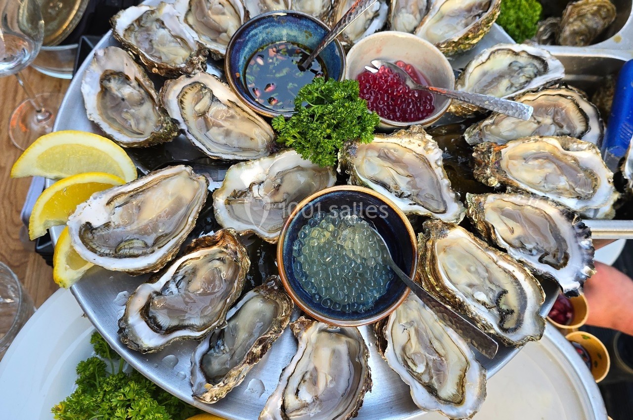 Plateau d'huîtres ouvertes servi avec citron, persil, et condiments dans des coupelles.