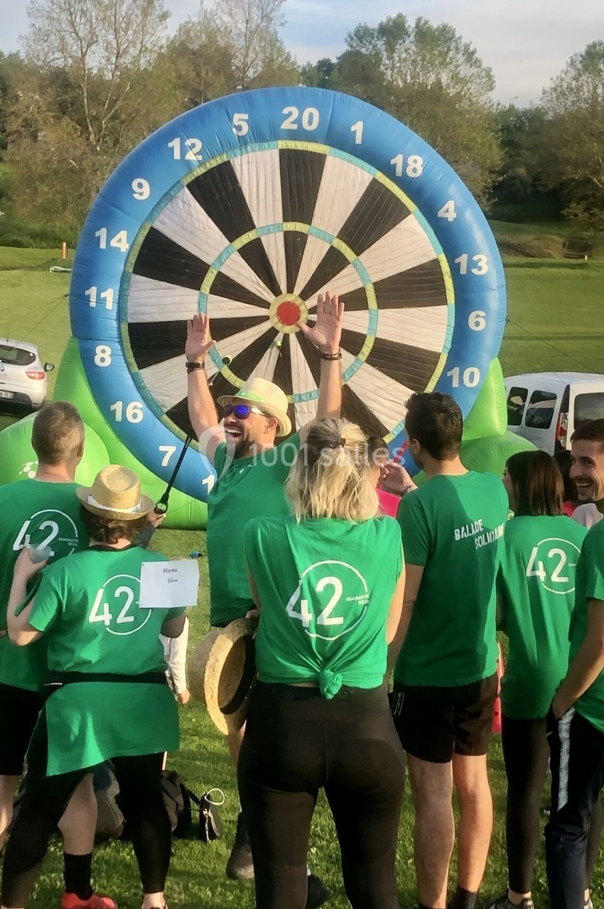 Un groupe de personnes en t-shirts verts participe à une activité de fléchettes géantes en plein air.
