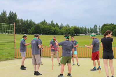 Un groupe de personnes en t-shirts verts participe à une activité de fléchettes géantes en plein air.
