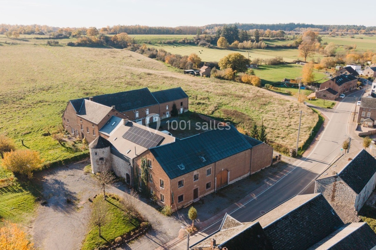 Vue aérienne d'un bâtiment en briques avec une tour, entouré de champs et de routes dans un paysage rural.