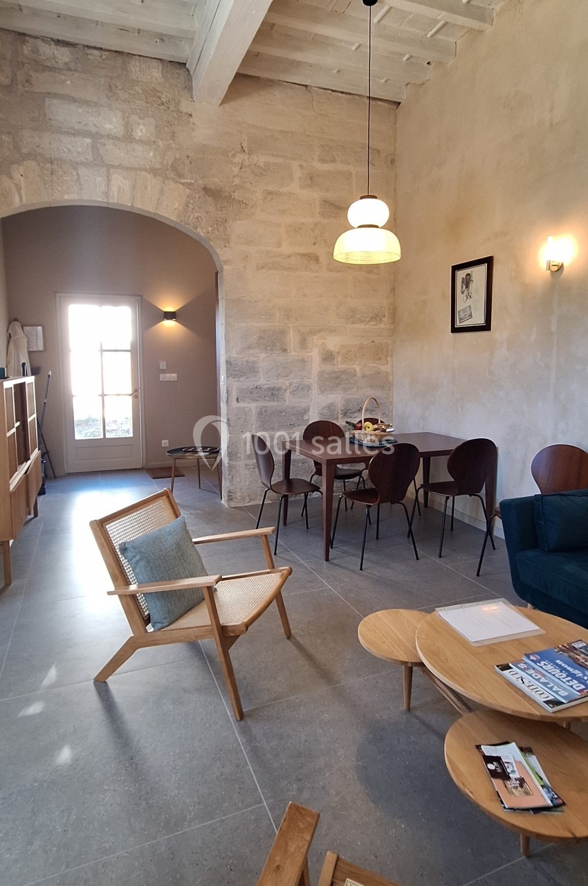 Salon lumineux avec murs en pierre, mobilier en bois, table à manger, fauteuils et grande porte vitrée donnant sur l…