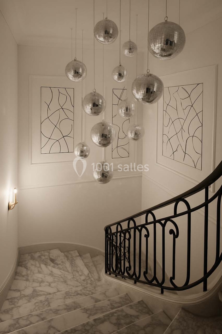 Escalier en marbre avec rampe en fer forgé, éclairé par des suspensions sphériques argentées et des appliques murales.