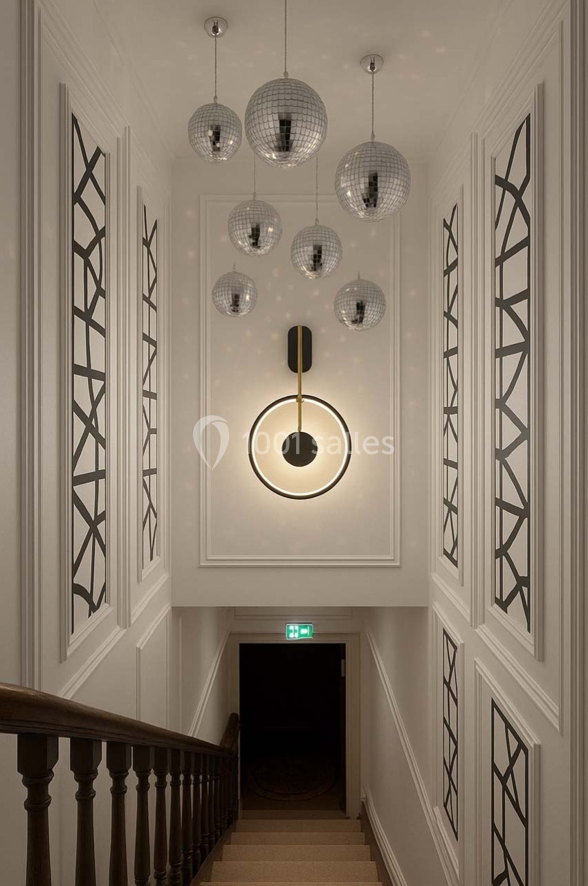 Escalier intérieur avec murs décorés de motifs géométriques, lustres sphériques et applique murale lumineuse.