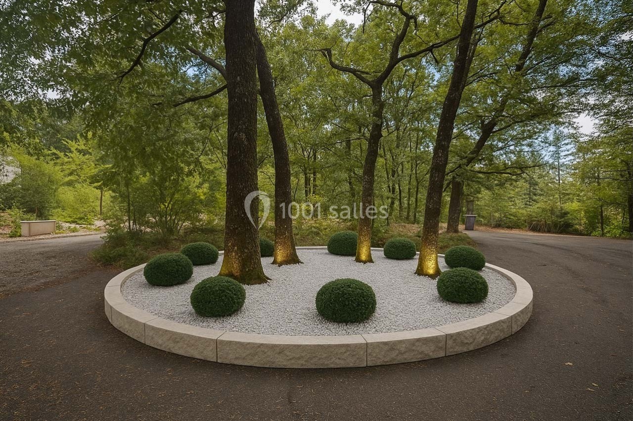 Aménagement paysager circulaire avec arbres éclairés, buissons taillés et gravier blanc, entouré d'une bordure en pierre.