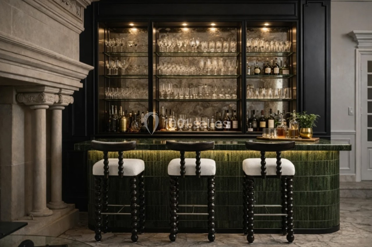 Bar élégant avec comptoir vert, tabourets noirs sculptés, étagères vitrées remplies de verres et bouteilles éclairées.