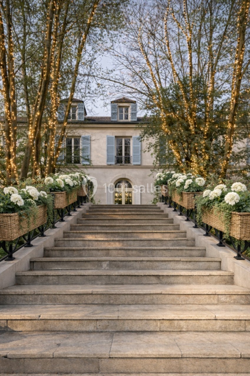 Escalier en pierre bordé de jardinières fleuries et éclairé par des guirlandes lumineuses, menant à une maison élégante.