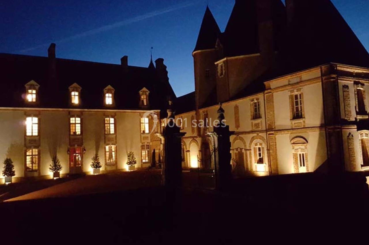 Façade d'un château éclairé la nuit, avec des fenêtres illuminées et un ciel sombre en arrière-plan.