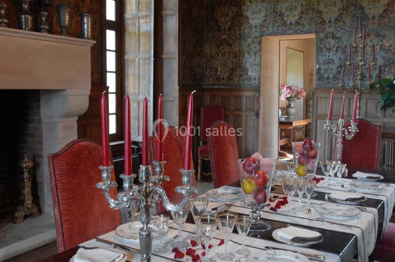 Salle à manger élégante avec table dressée, chandeliers argentés, bougies rouges et décorations florales.