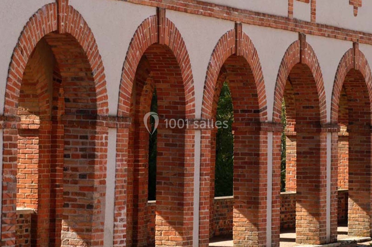 Arcades en briques rouges et blanches d'un bâtiment, éclairées par la lumière naturelle.