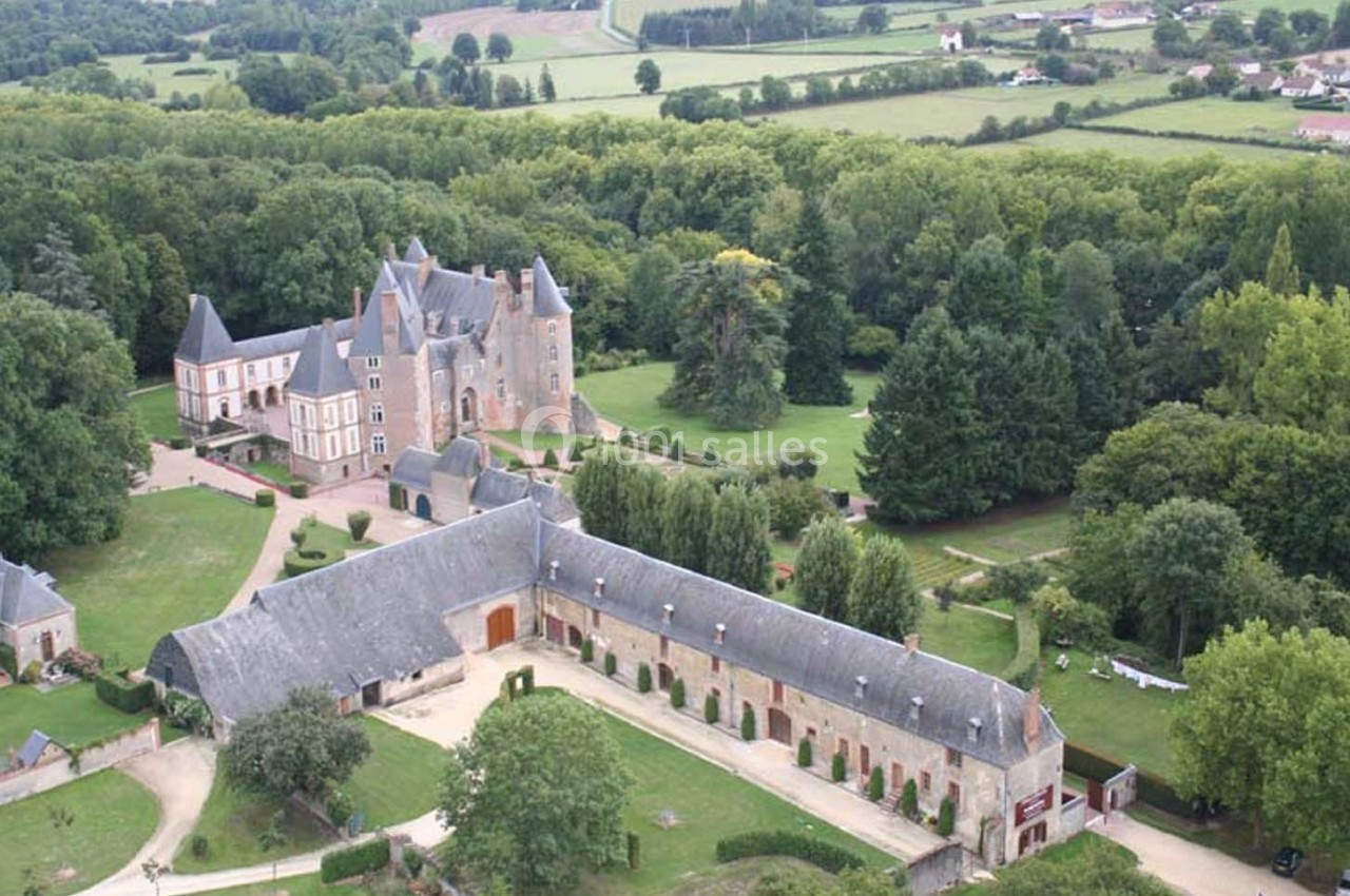 Vue aérienne d'un château entouré de bâtiments annexes, de jardins et de forêts dans une campagne verdoyante.