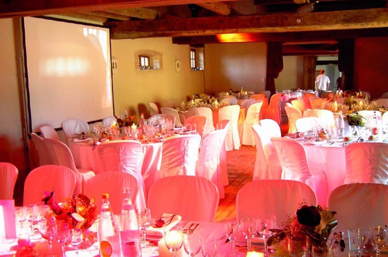 Salle de réception décorée avec des tables rondes dressées, nappes blanches et lumière chaleureuse.