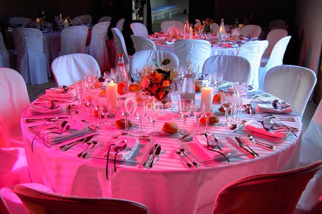 Table ronde élégamment dressée avec nappes blanches, couverts, verres, bougies et décoration florale dans une ambiance…