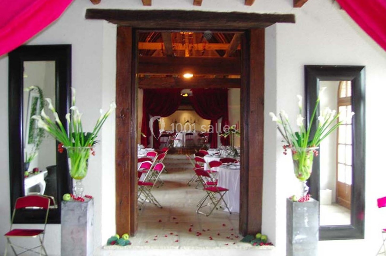 Entrée d'une salle de réception décorée avec des rideaux rouges, des fleurs blanches et des tables dressées.