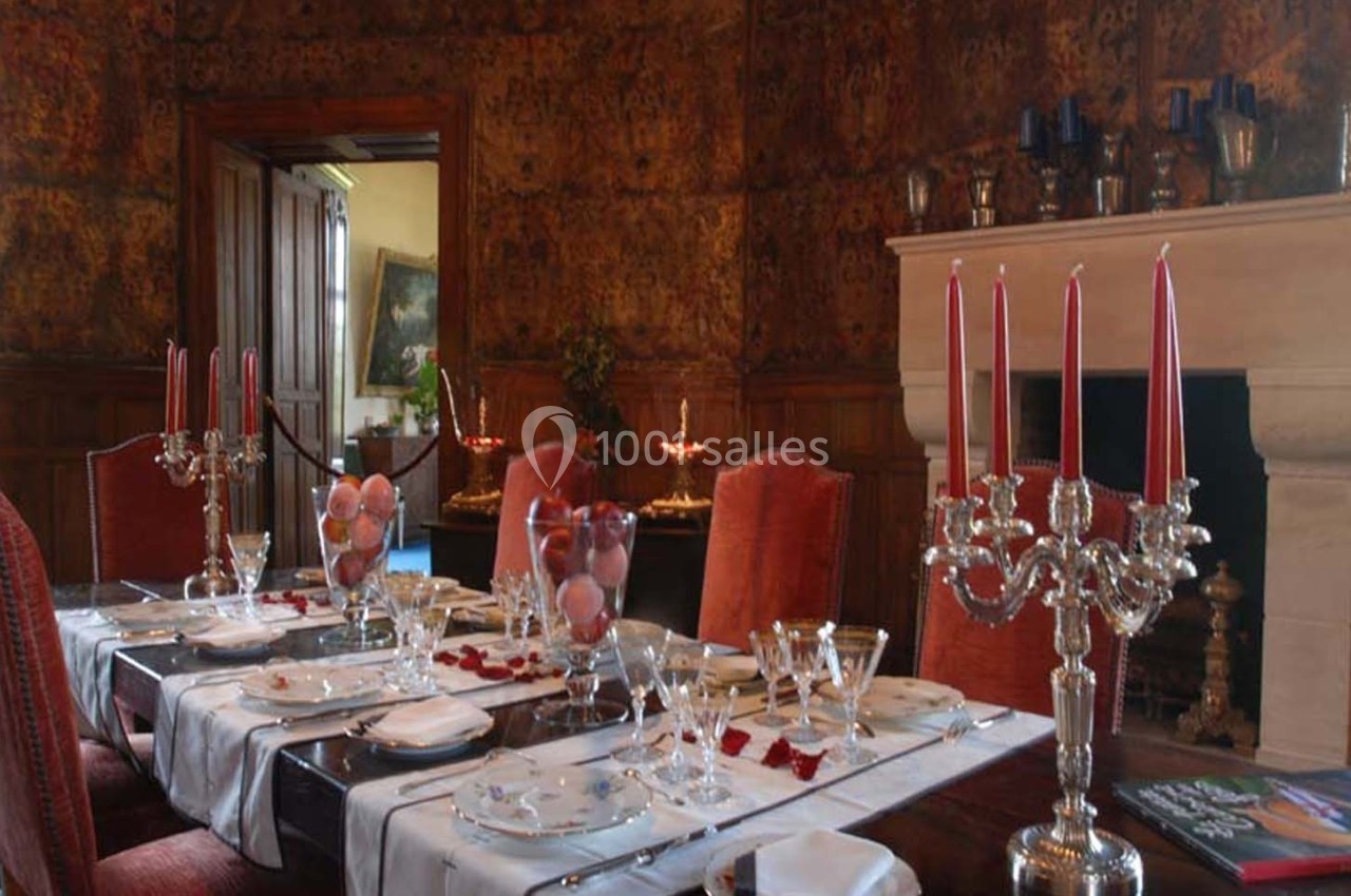 Salle à manger élégante avec table dressée, chandeliers argentés, bougies rouges et décoration raffinée.