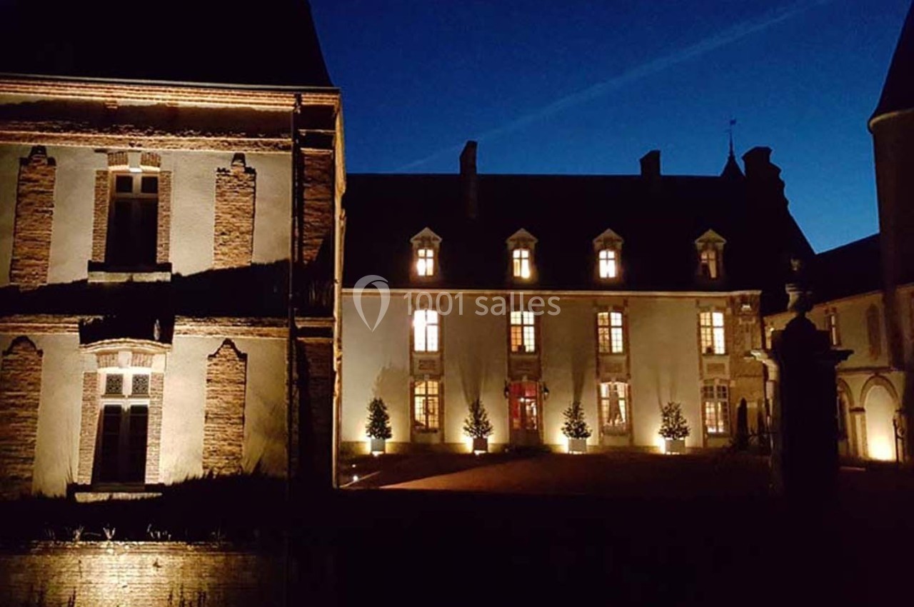 Façade éclairée d'un château historique en soirée, avec un ciel nocturne dégagé en arrière-plan.