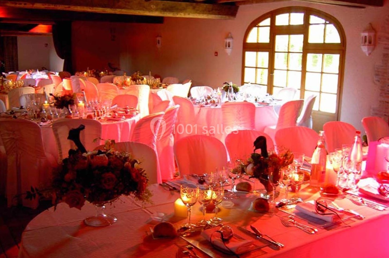 Salle de réception décorée avec des tables dressées, nappes blanches, bouquets de fleurs et éclairage chaleureux.