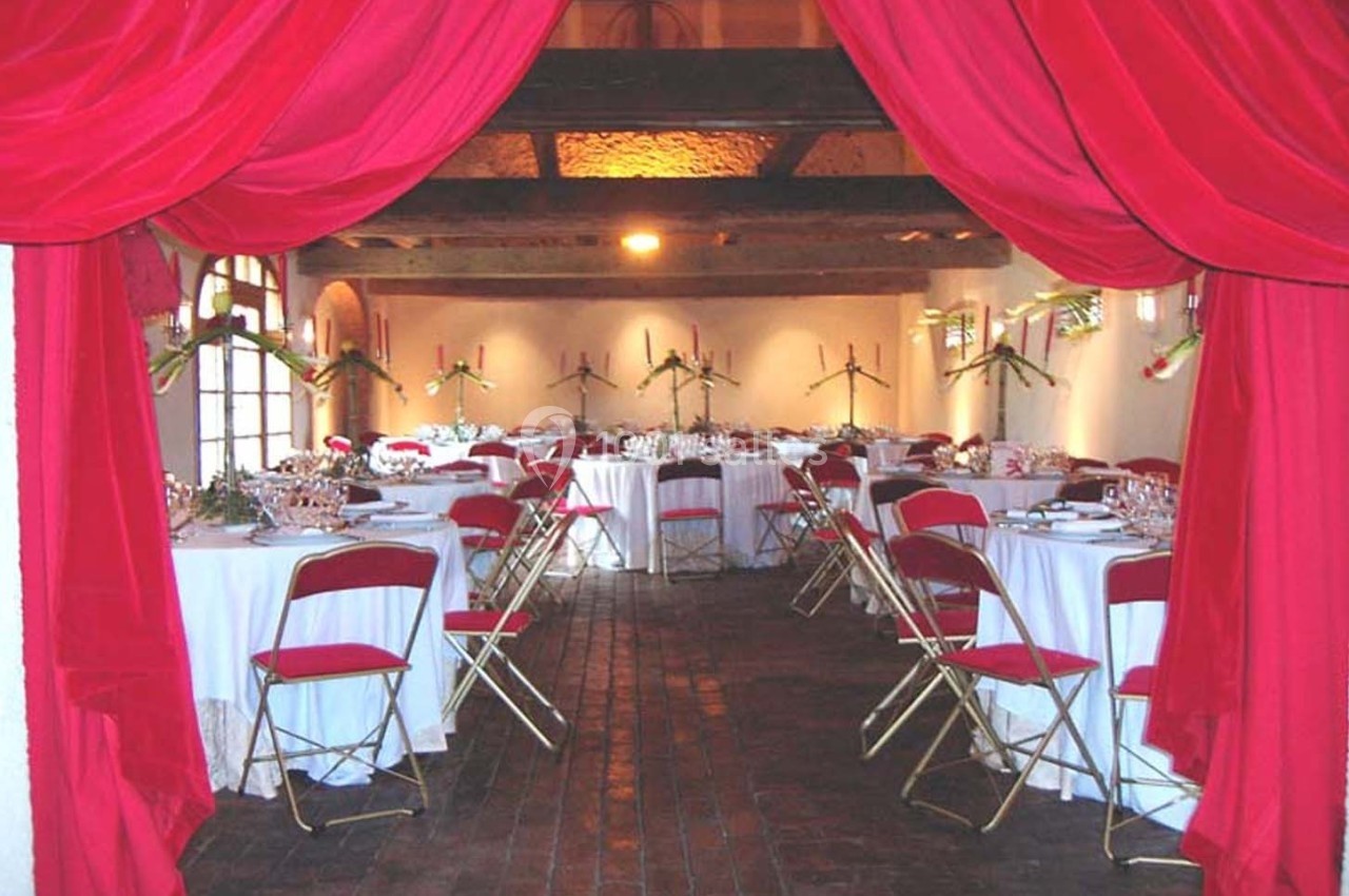Salle de réception décorée avec des nappes blanches, des chaises rouges et des rideaux rouges encadrant l'entrée.