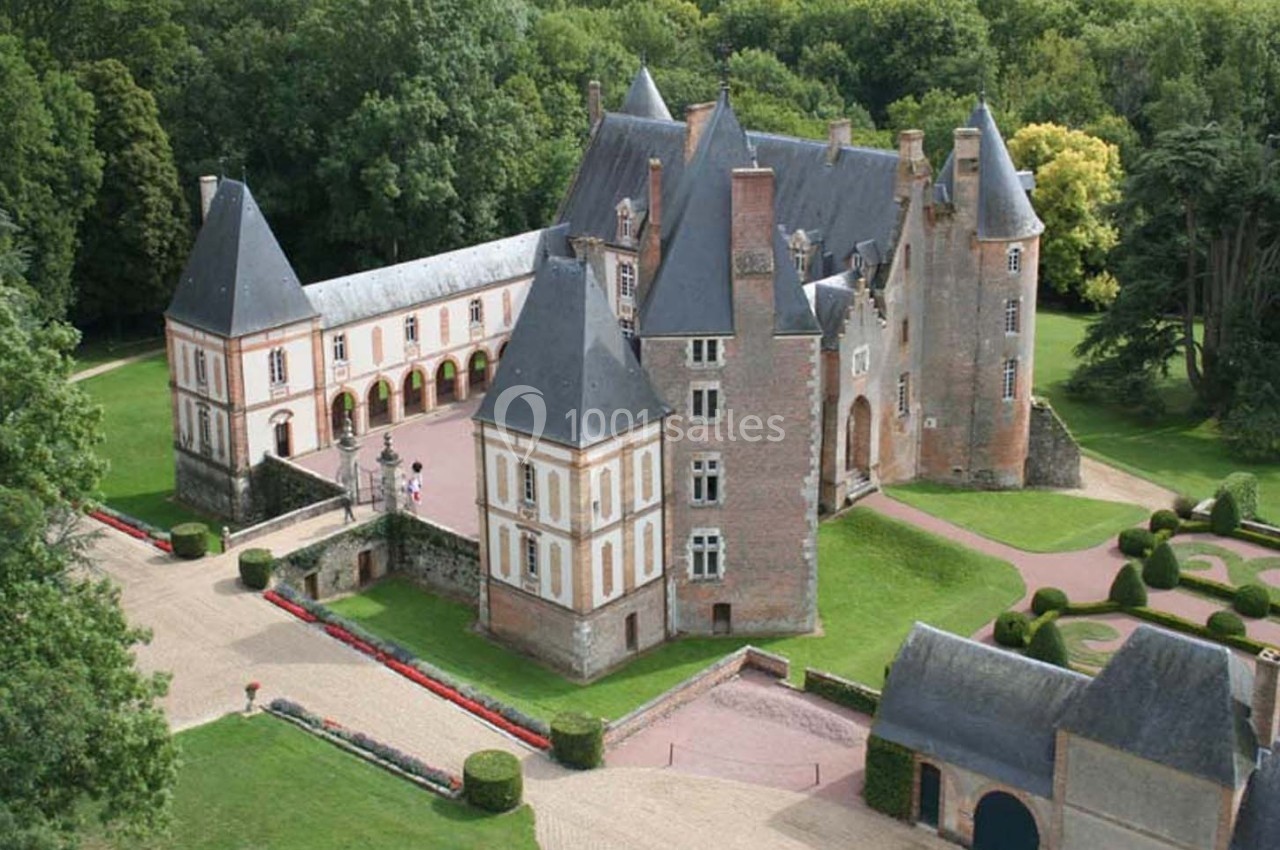 Vue aérienne d'un château en briques entouré de jardins, d'arbres et d'une cour pavée.