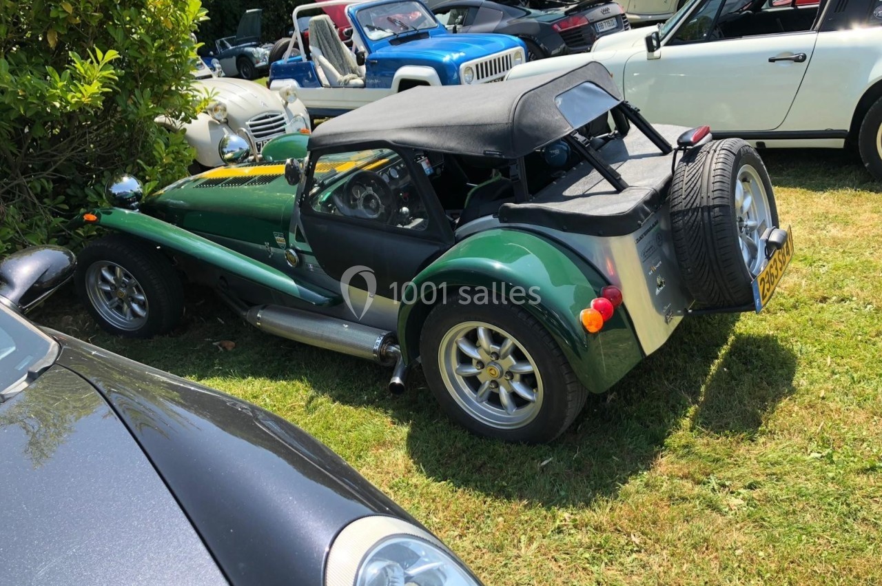 Voiture de sport verte et noire garée sur une pelouse, entourée d'autres véhicules lors d'un rassemblement.