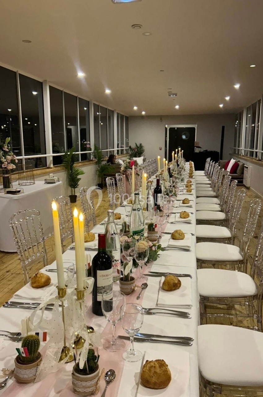 Table dressée pour un dîner élégant avec chandeliers, bouteilles de vin et décorations, dans une salle lumineuse.