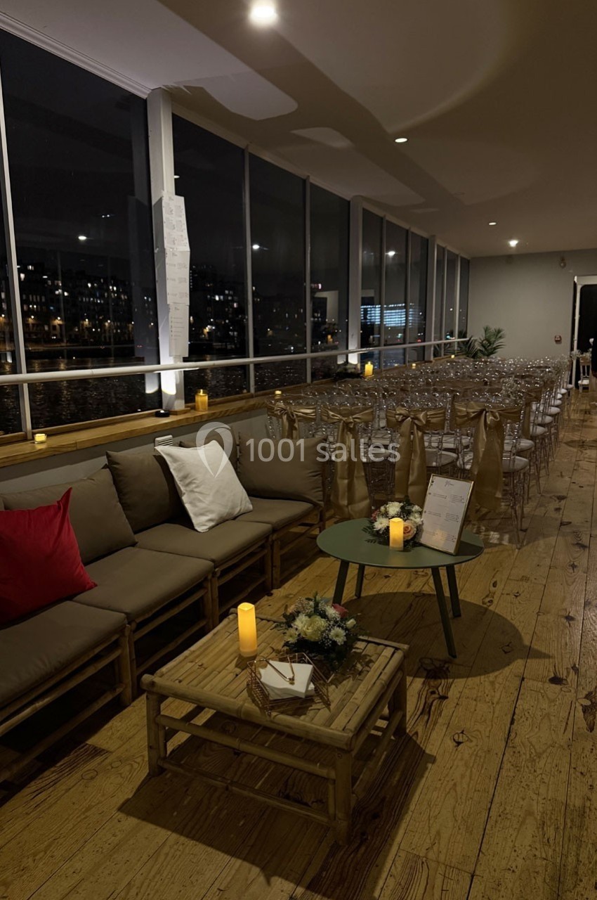 Salle de réception en soirée avec des chaises alignées, un canapé, des tables basses en bois et des bougies allumées.