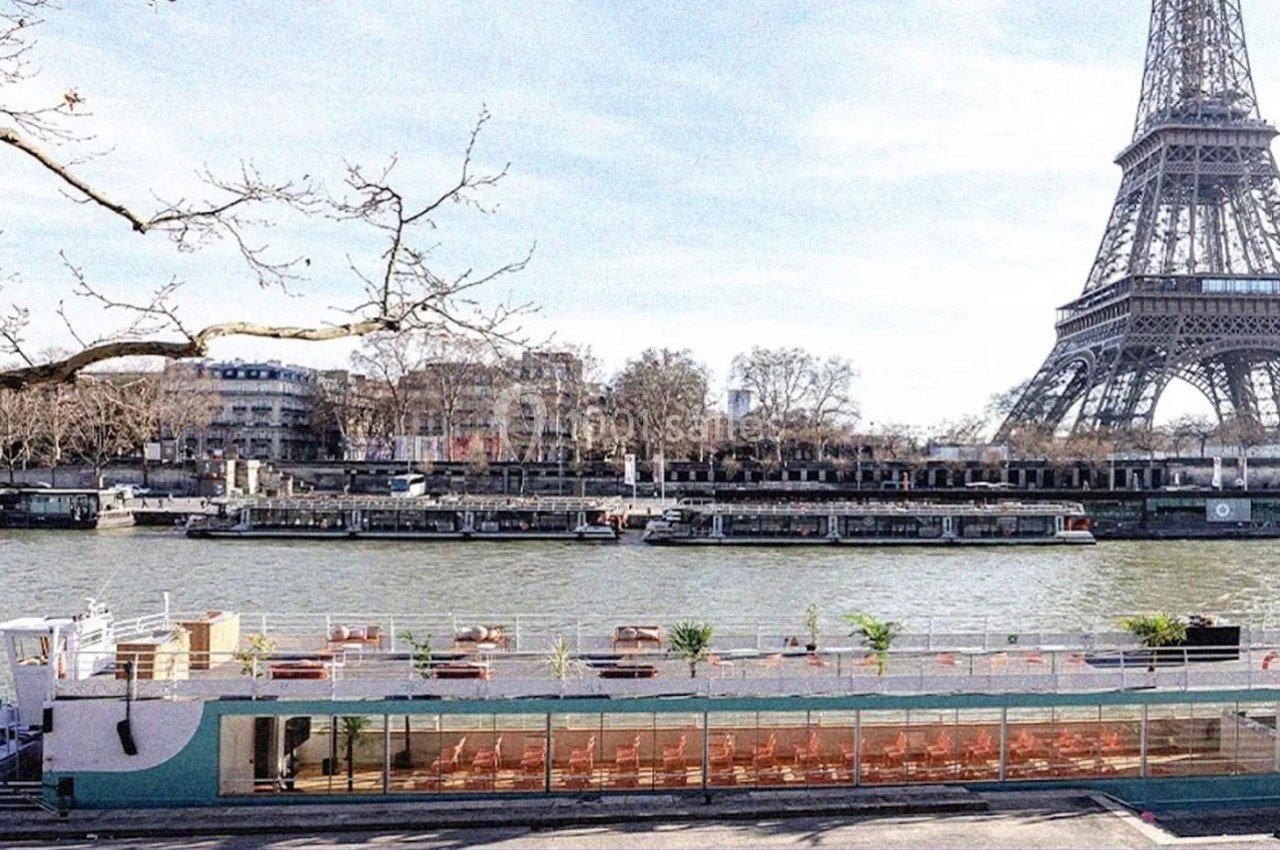 Bateau amarré sur la Seine avec terrasse aménagée, vue sur la Tour Eiffel et bâtiments en arrière-plan.