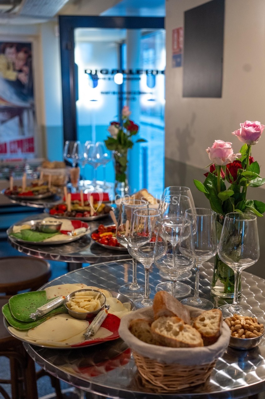 Tables dressées avec des assiettes de fromages, pain, verres à vin et décorations florales dans un cadre convivial.