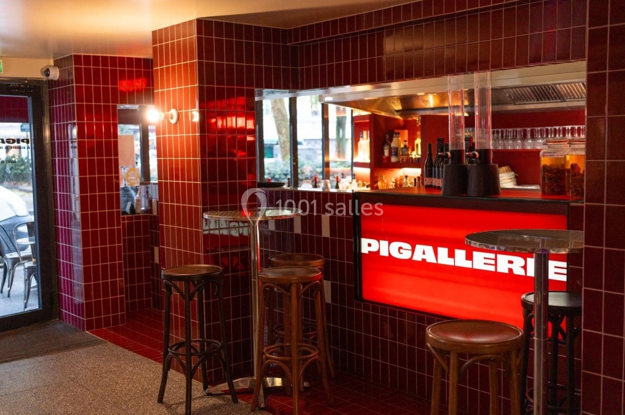 Intérieur d'un bar avec murs en carrelage rouge, comptoir lumineux et tabourets en bois autour de tables hautes.