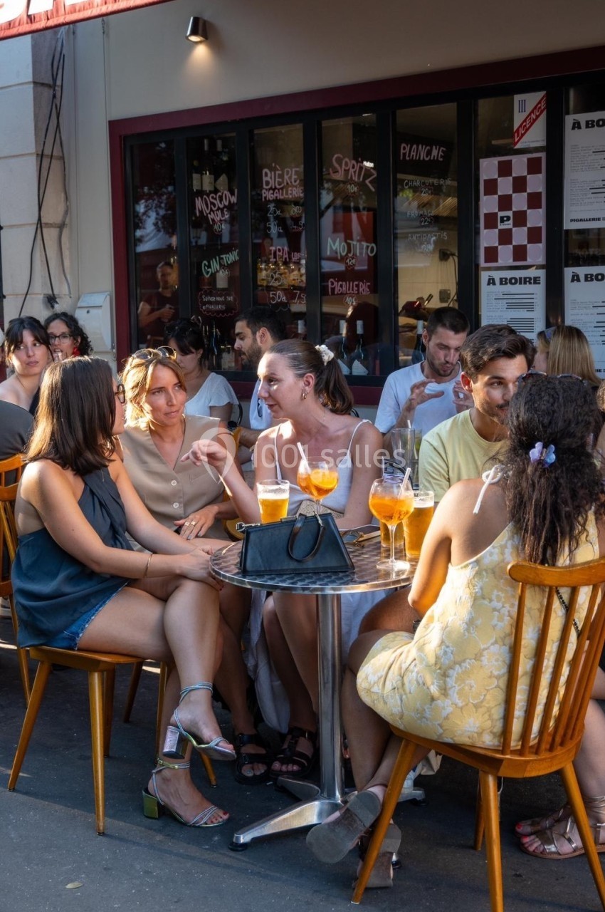 Des personnes discutent autour de tables en terrasse, avec des boissons servies dans un cadre animé et ensoleillé.