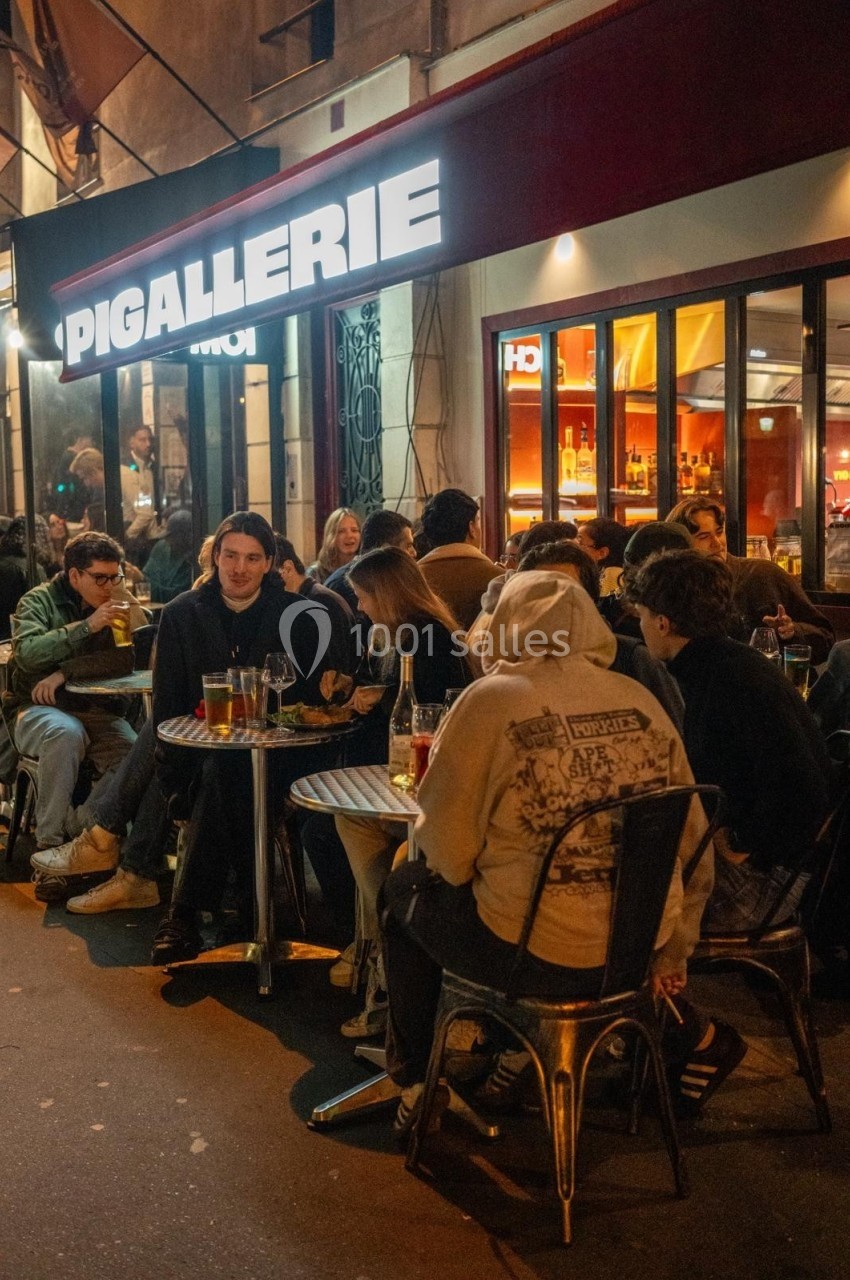 Des personnes assises à des tables en terrasse d'un café animé, éclairé par des lumières nocturnes.