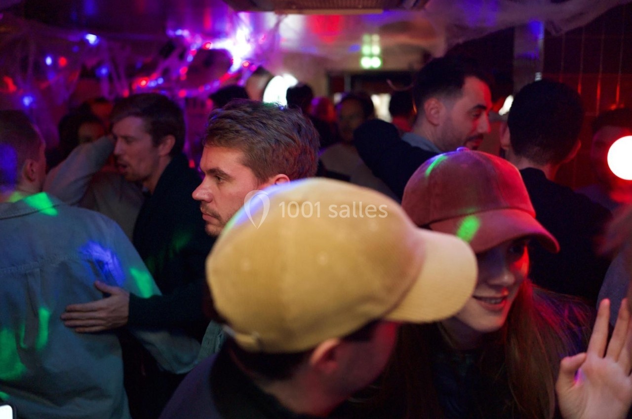 Groupe de personnes discutant et dansant dans un espace sombre décoré de lumières colorées et toiles d'araignée.