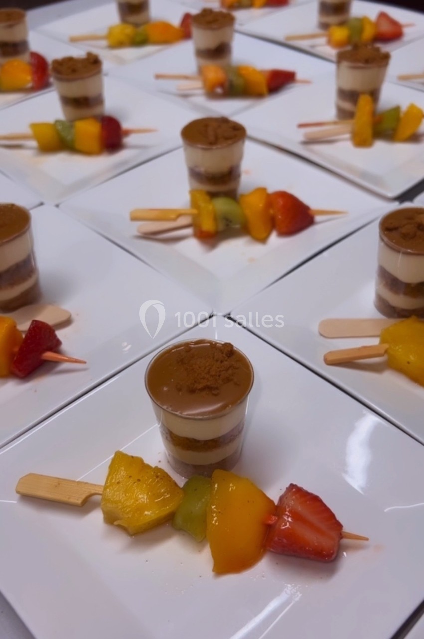 Desserts individuels en verrines accompagnés de brochettes de fruits colorés disposés sur des assiettes blanches.