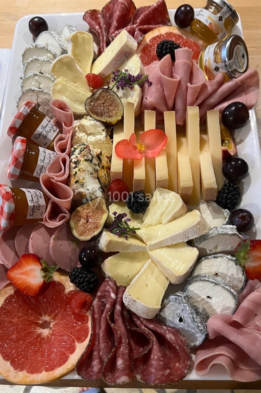Plateau de charcuteries, fromages variés, fruits frais, confitures et décorations florales sur une table en bois.
