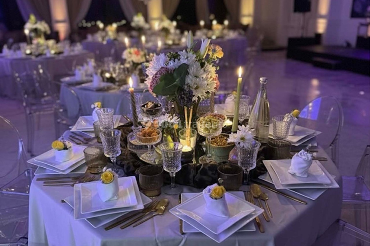 Table élégamment dressée avec vaisselle raffinée, fleurs, bougies allumées et décorations pour un événement festif.