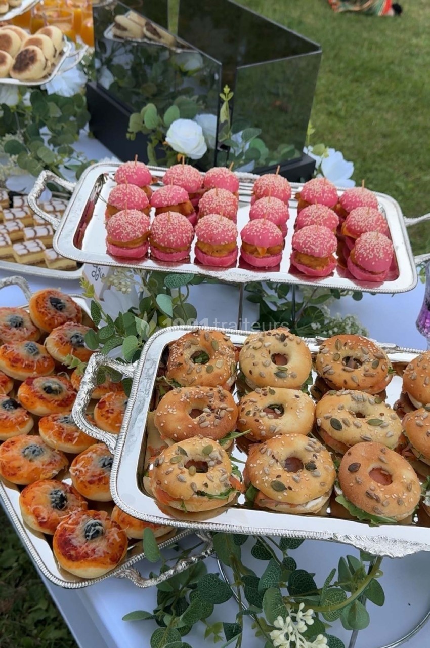 Plateaux de mini-pâtisseries et viennoiseries variées disposés sur une table décorée de feuillage.
