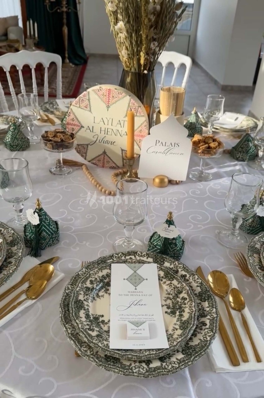 Table élégamment dressée avec vaisselle ornée, couverts dorés, menus et décorations raffinées sur nappe blanche.