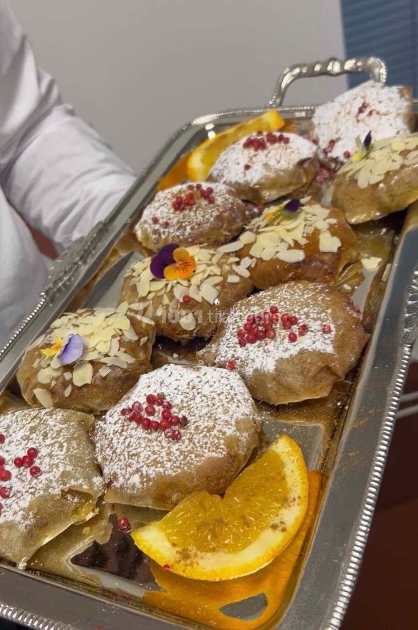 Plateau de pâtisseries garnies d'amandes, sucre glace, fleurs comestibles et tranches d'orange en décoration.