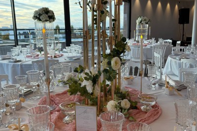 Table de réception élégamment dressée avec chandeliers, fleurs pourpres et vaisselle raffinée dans une salle lumineuse.