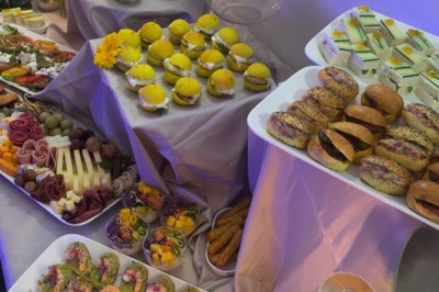 Table de réception élégamment dressée avec chandeliers, fleurs pourpres et vaisselle raffinée dans une salle lumineuse.