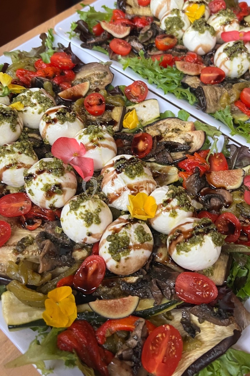 Plateaux de salade garnis de mozzarella, tomates cerises, légumes grillés, pesto, fleurs comestibles et vinaigre balsamique.